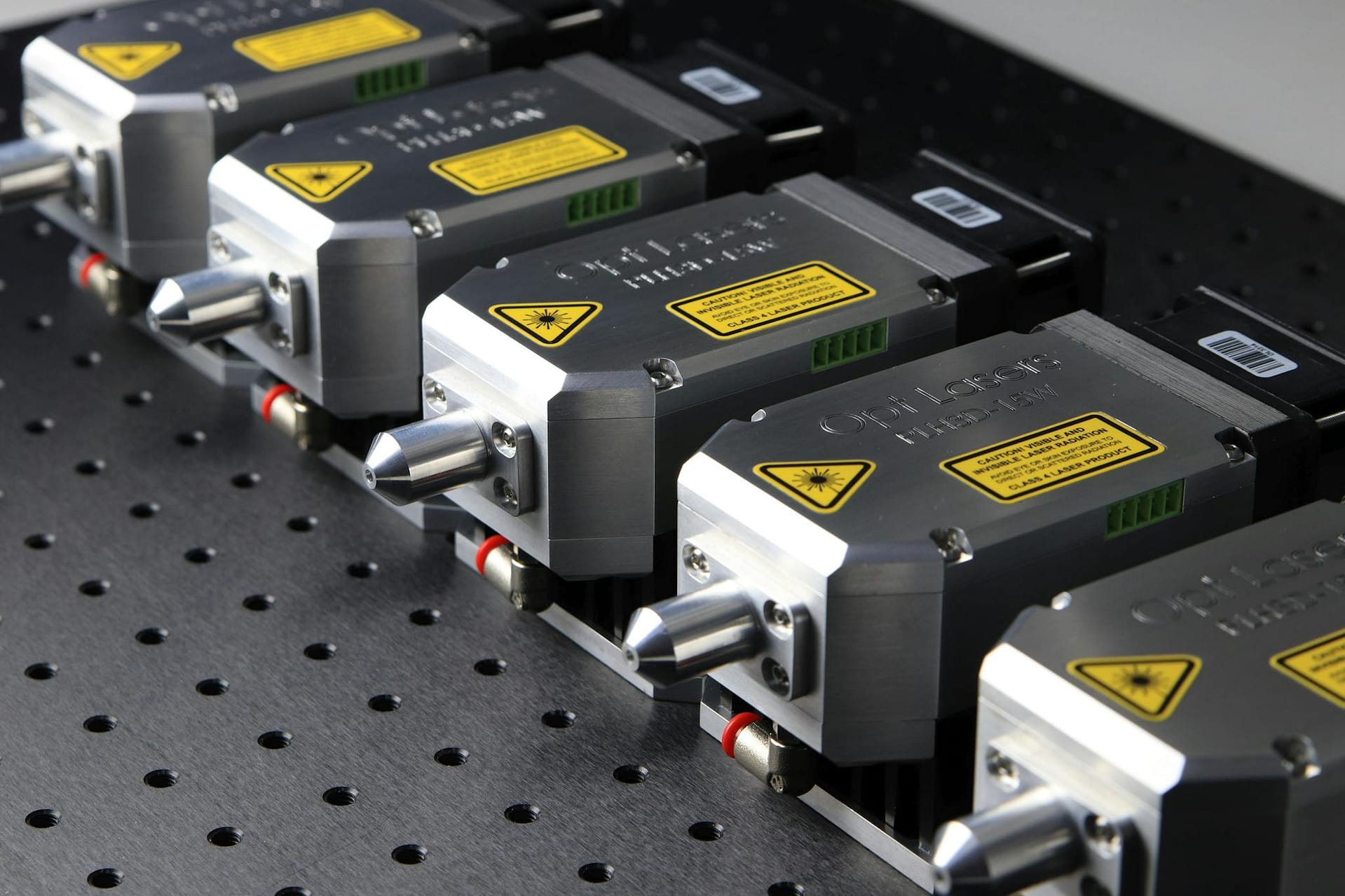 Detailed close-up of industrial laser modules with warning labels on a perforated metal surface.